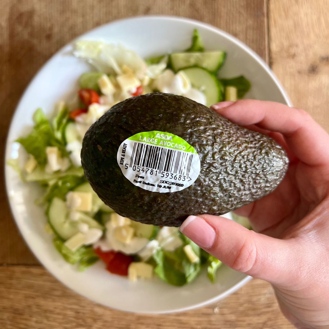 Hand holding an avocado with a date label.