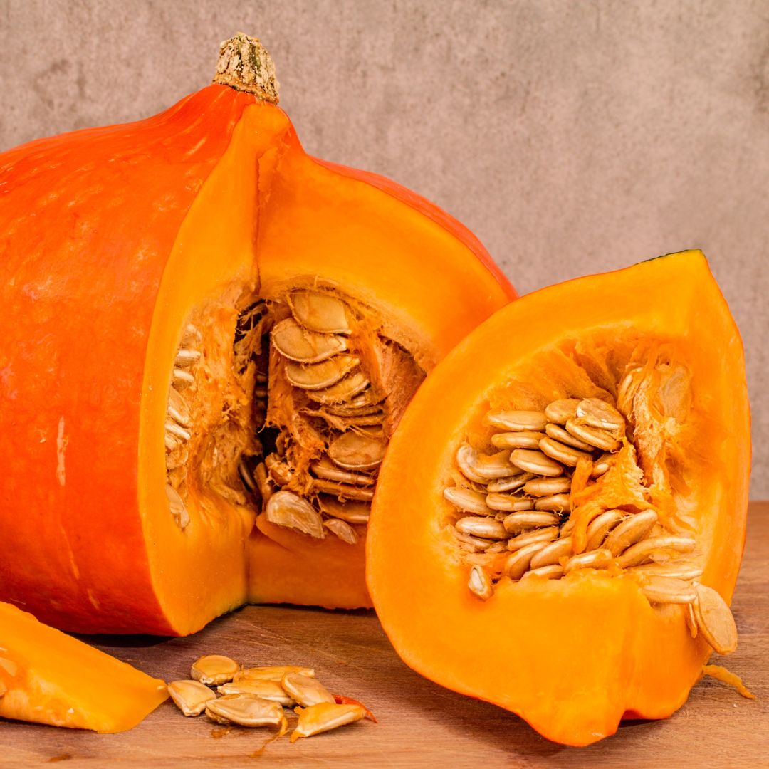 An orange pumpkin with a slice removed revealing its seeds and flesh.